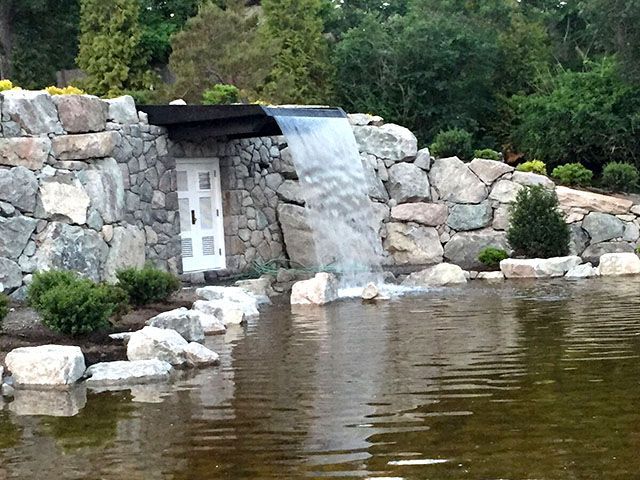 A waterfall in the middle of a pond in front of a stone wall