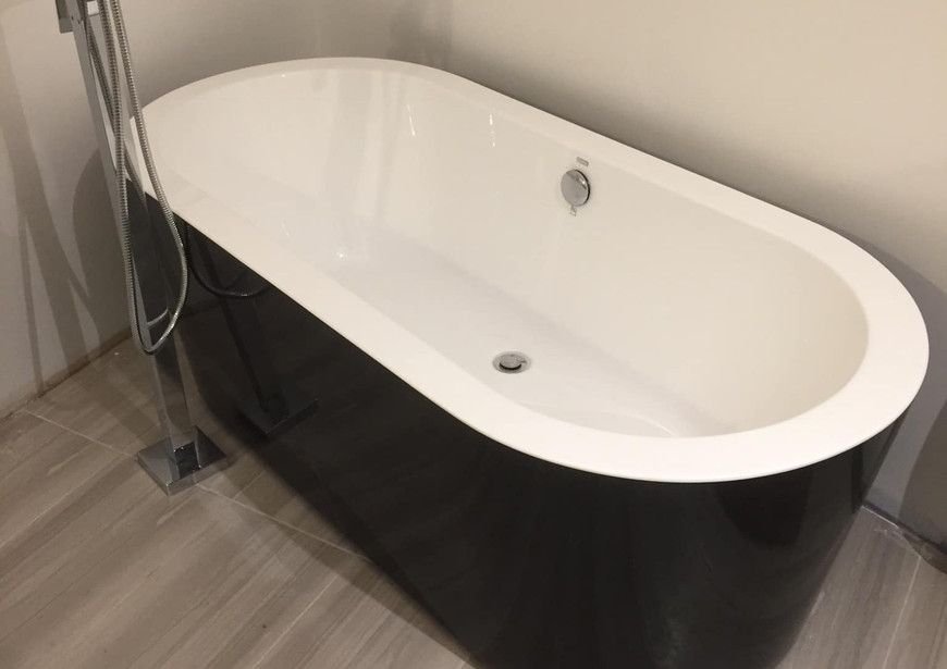 Une baignoire noire et blanche est posée sur un plancher en bois dans une salle de bain.