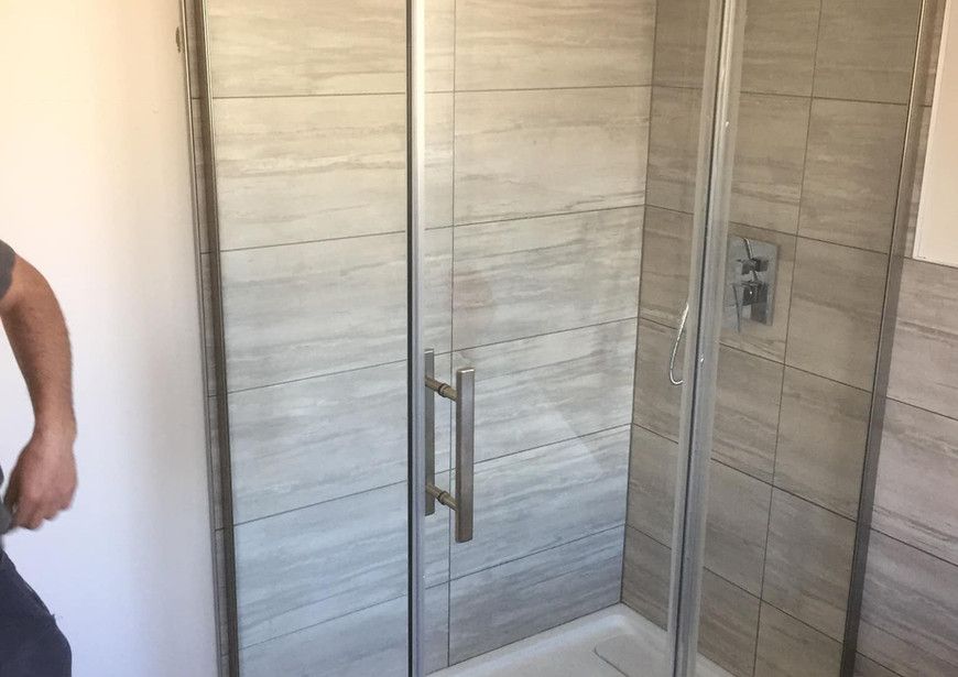 Une femme se tient dans une salle de bain à côté d'une cabine de douche.