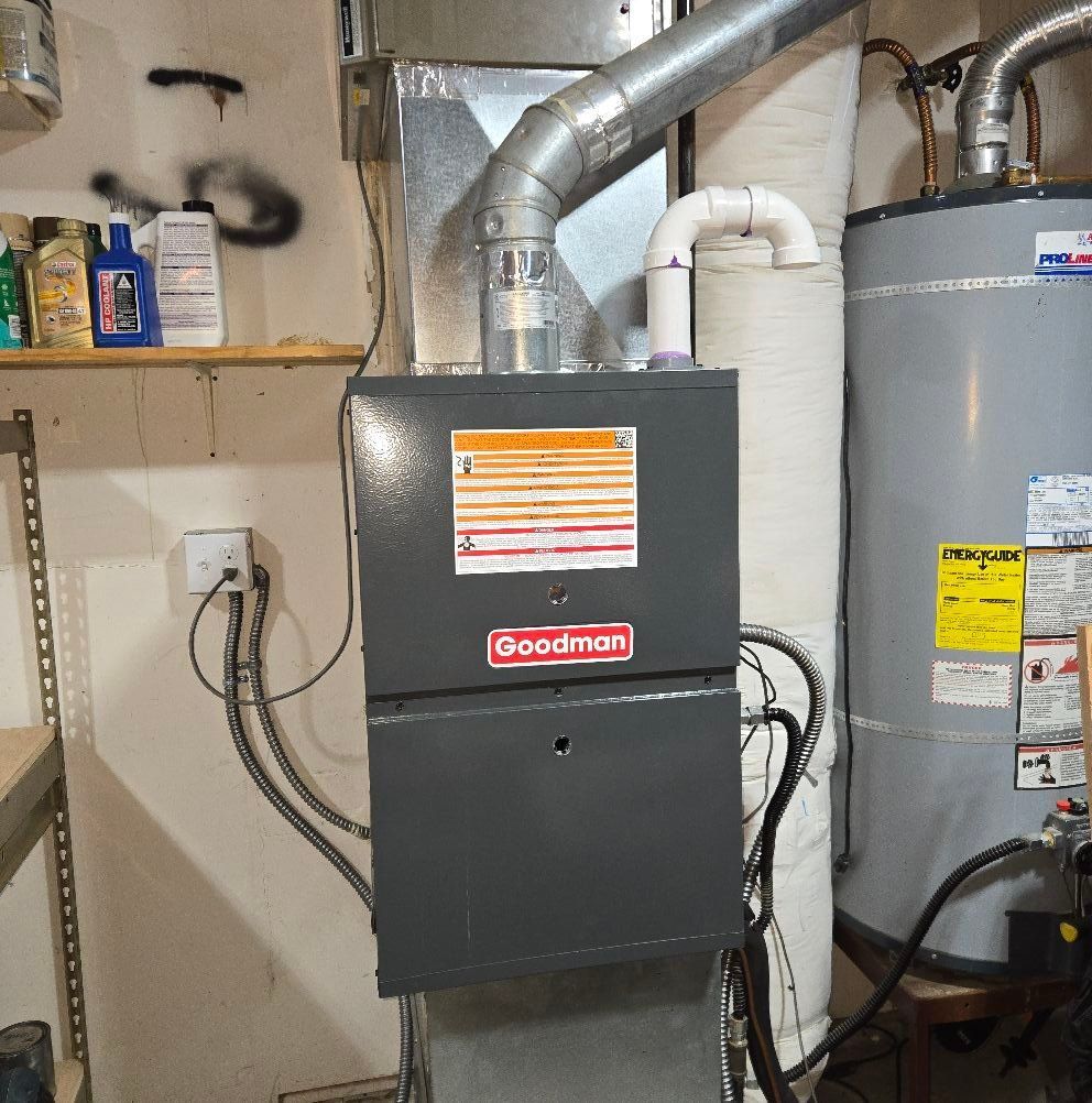 Furnace and hot water heater in a basement. Goodman furnace, metal ductwork, and white PVC exhaust pipe.