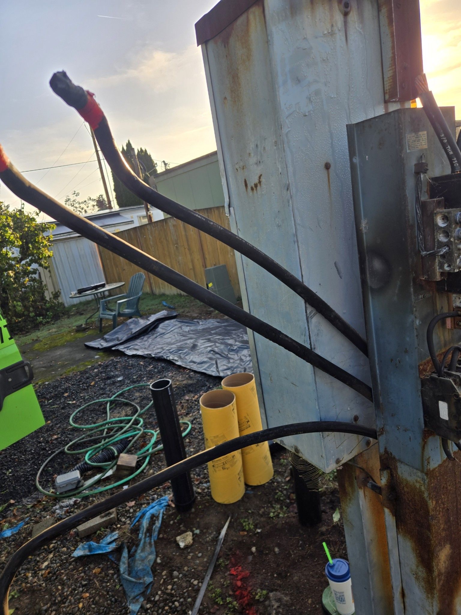 Electrical transformer with black cables and protective yellow cylinders outdoors.