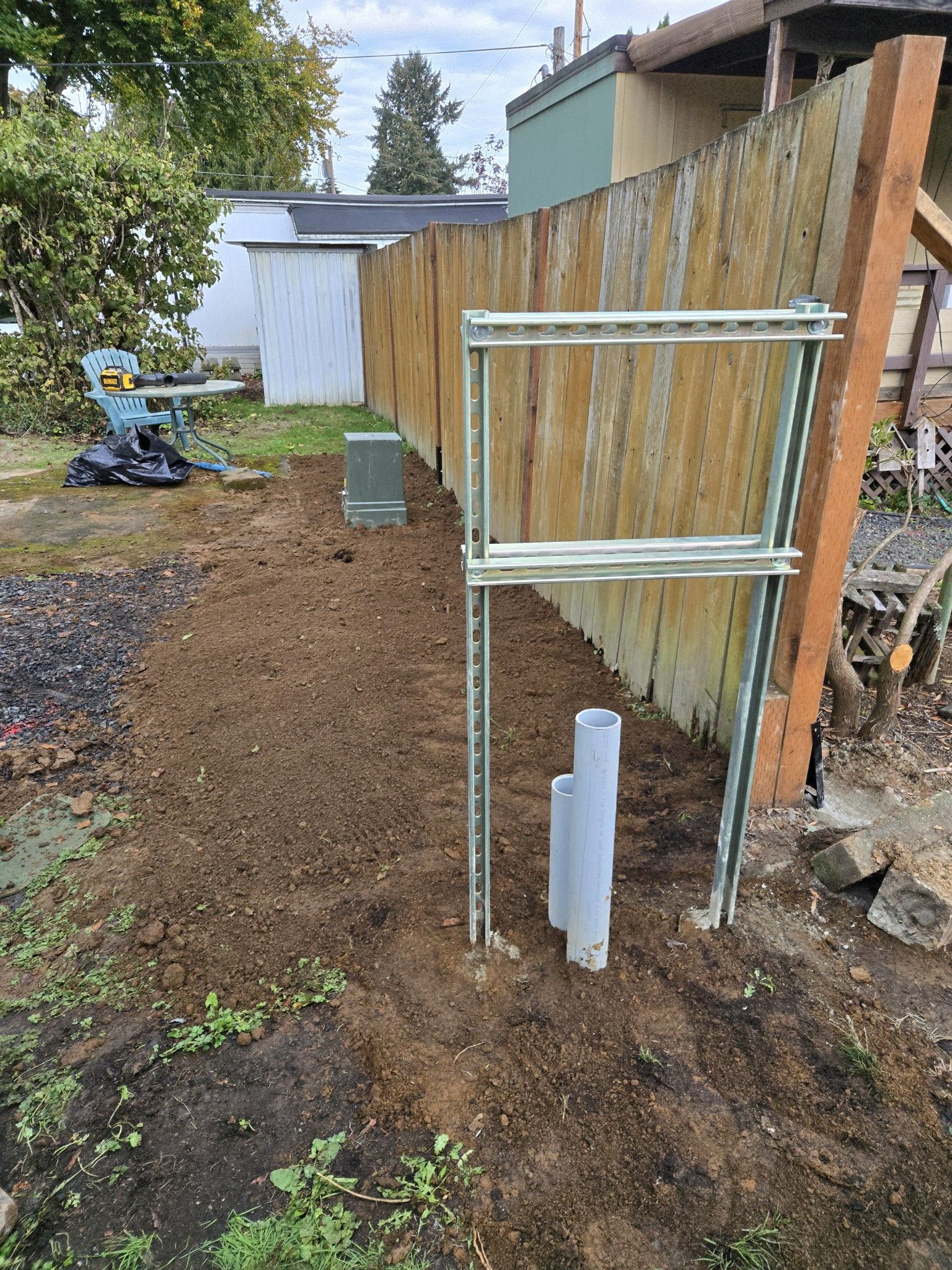 Backyard with a trench, electrical conduit, and metal frame next to a wooden fence and dirt.