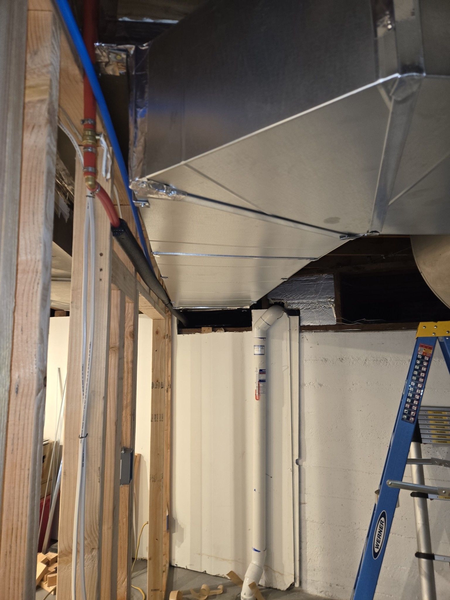 Basement with ductwork, plumbing, and a ladder. Framing on the left. White and gray tones.