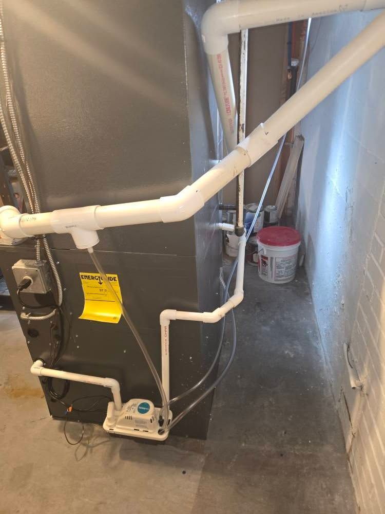 Furnace with white PVC pipes and condensate pump in a basement setting.