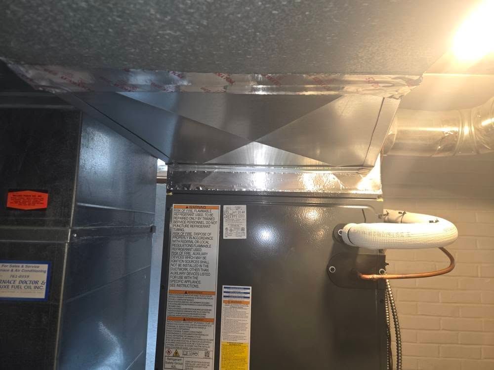 HVAC unit with ductwork in a room. Metallic silver color, attached to a ceiling.