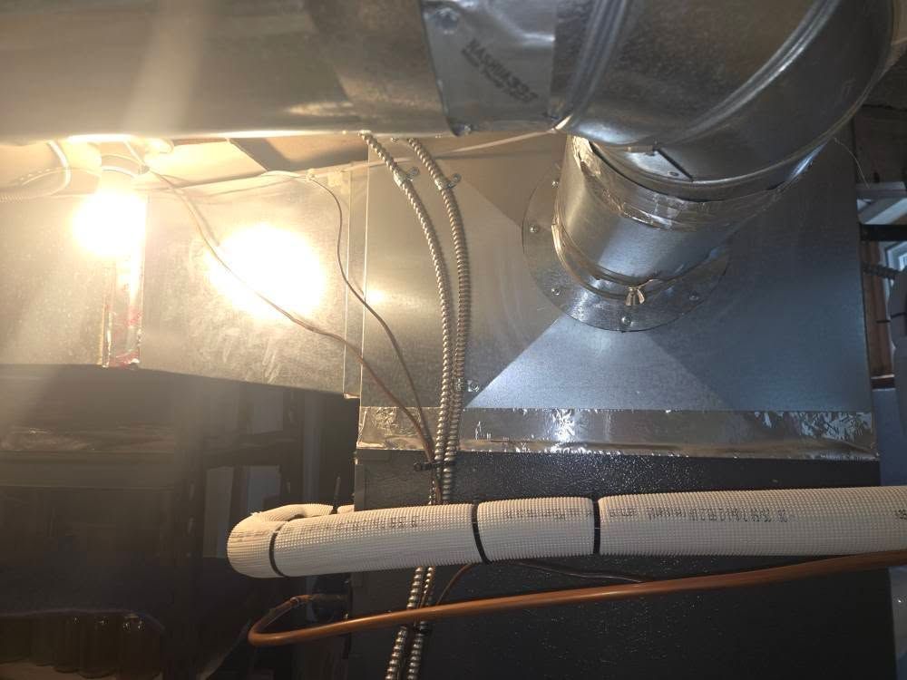 HVAC ductwork, lit by two overhead bulbs, with electrical wiring and a white pipe secured below.