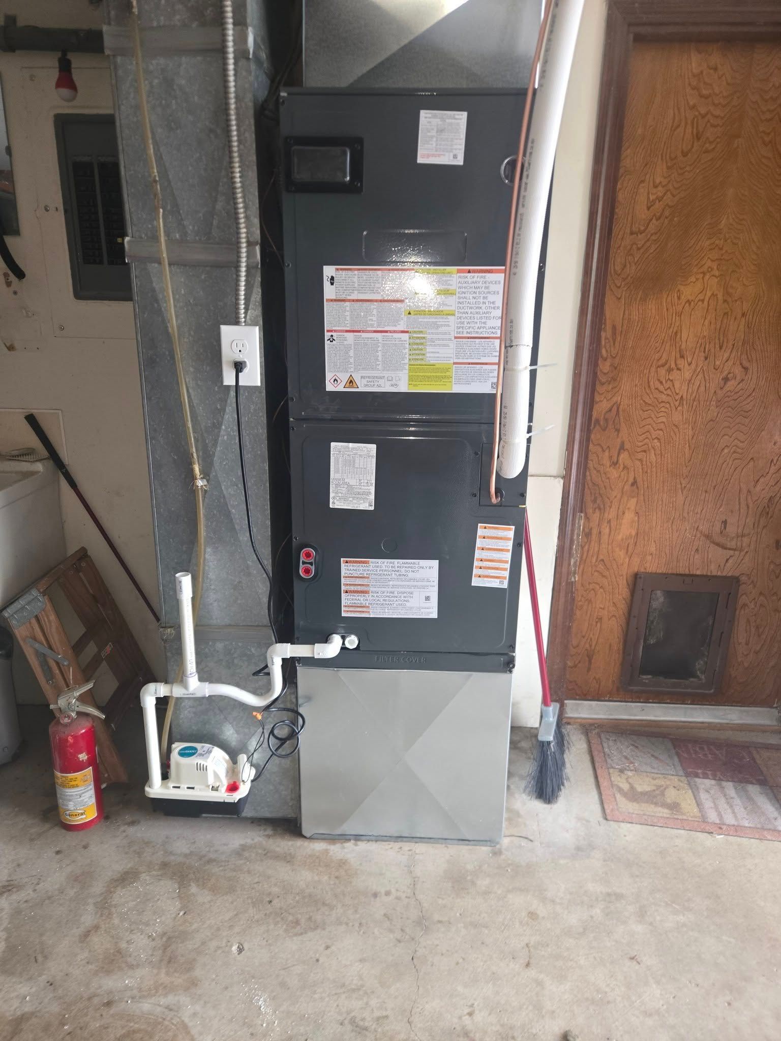 Furnace unit in a utility room with attached pipes and fire extinguisher nearby.