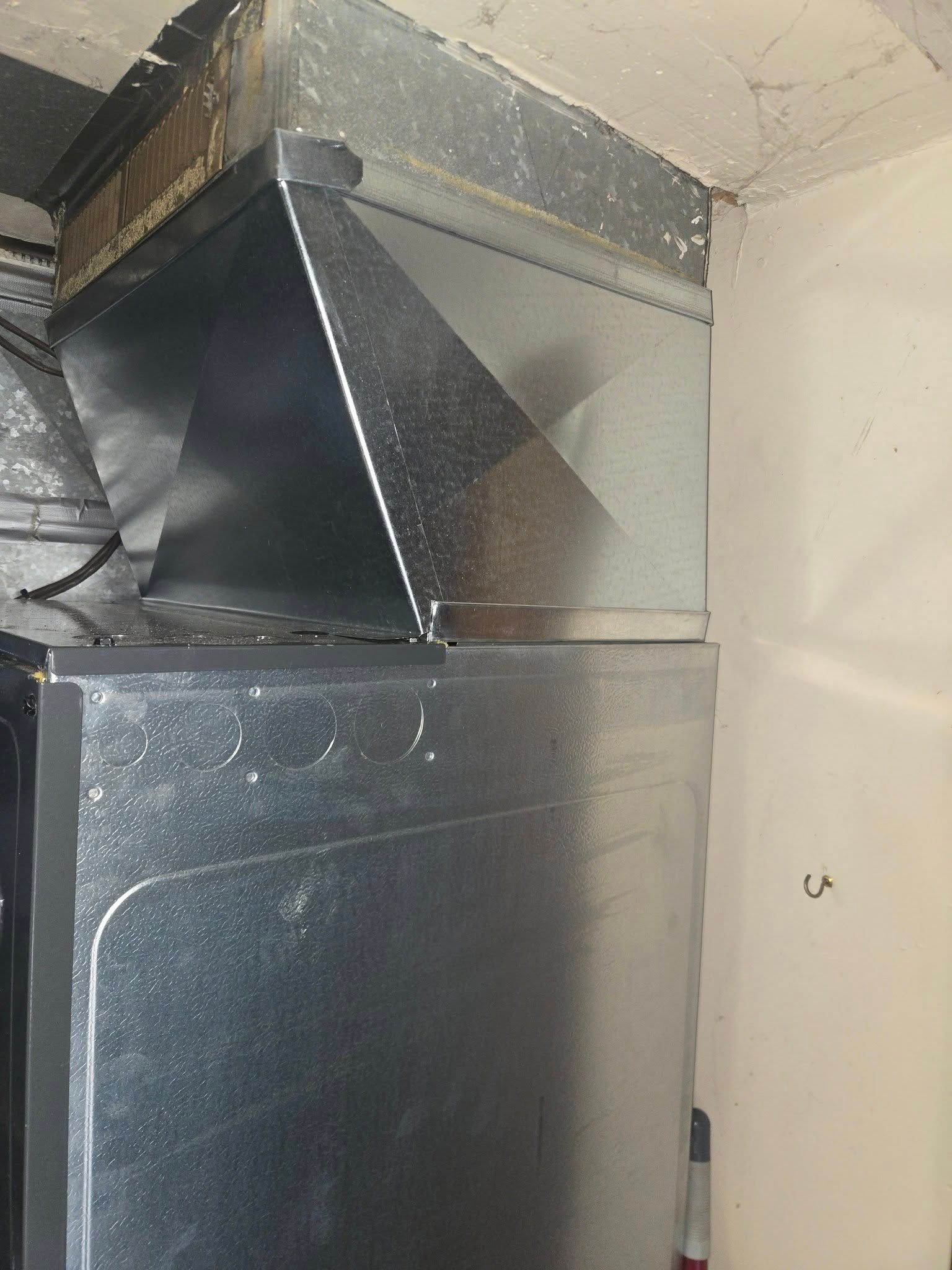 Metal ductwork attached to a furnace, located in a corner against a white wall.