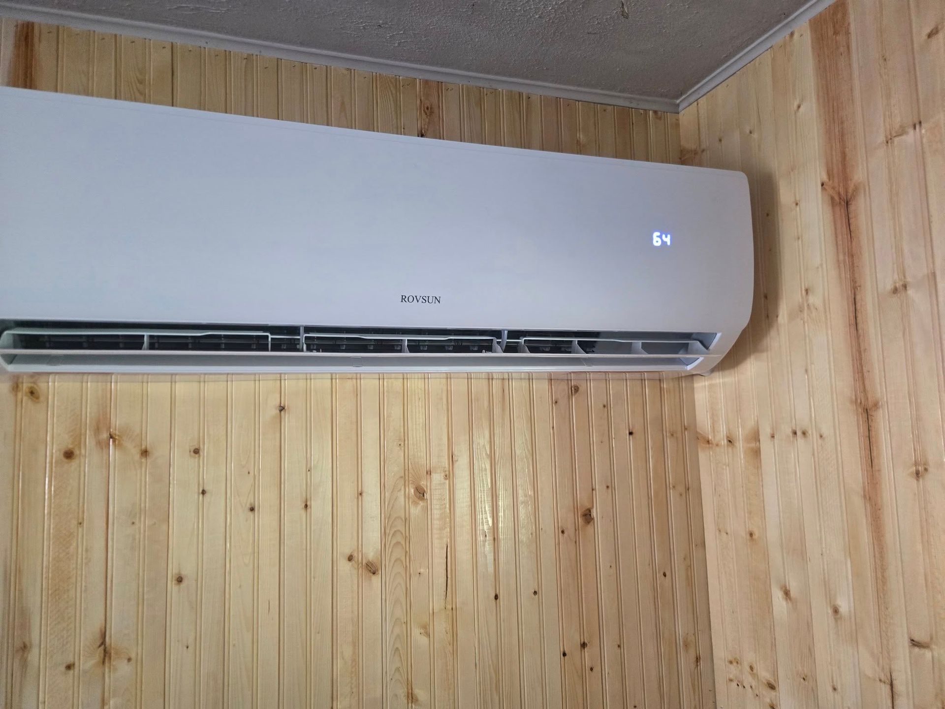 White air conditioner mounted on a wood-paneled wall.
