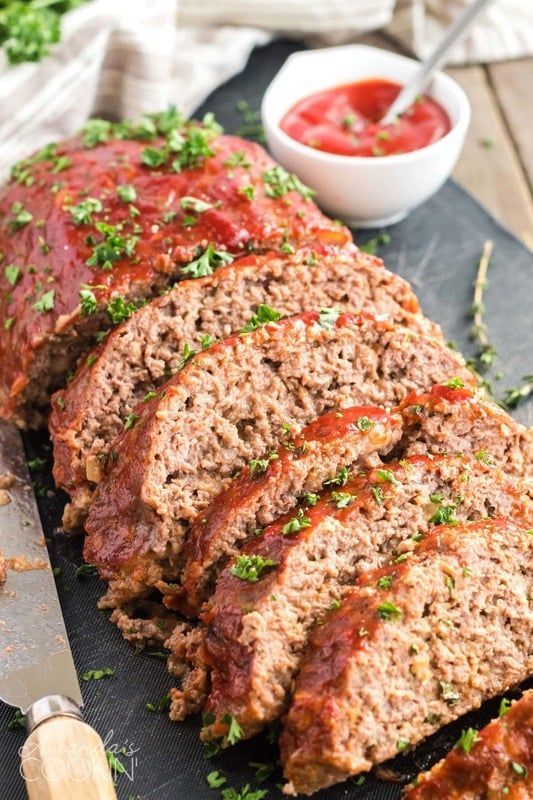 A meatloaf is sitting on a cutting board next to a bowl of ketchup.