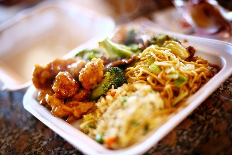 A styrofoam container filled with noodles , broccoli , and chicken on a table.