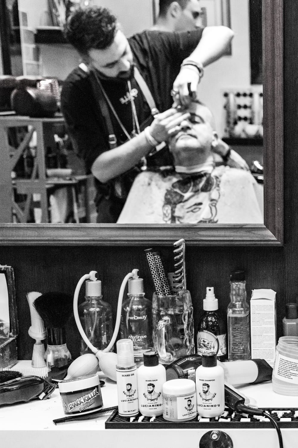 Un barbiere taglia i capelli a un cliente in un salone, con i prodotti per la cura della persona esposti sul bancone.