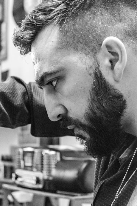 Primo piano in bianco e nero di un uomo barbuto che si sporge in avanti in un'officina, concentrato su un compito.