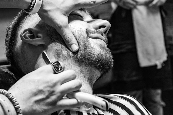 Il barbiere rifinisce la barba di un uomo con il rasoio elettrico, tenendogli fermo il viso.