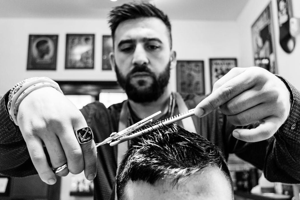 Un barbiere taglia i capelli a un uomo con le forbici in una scena in bianco e nero ambientata in una barberia.