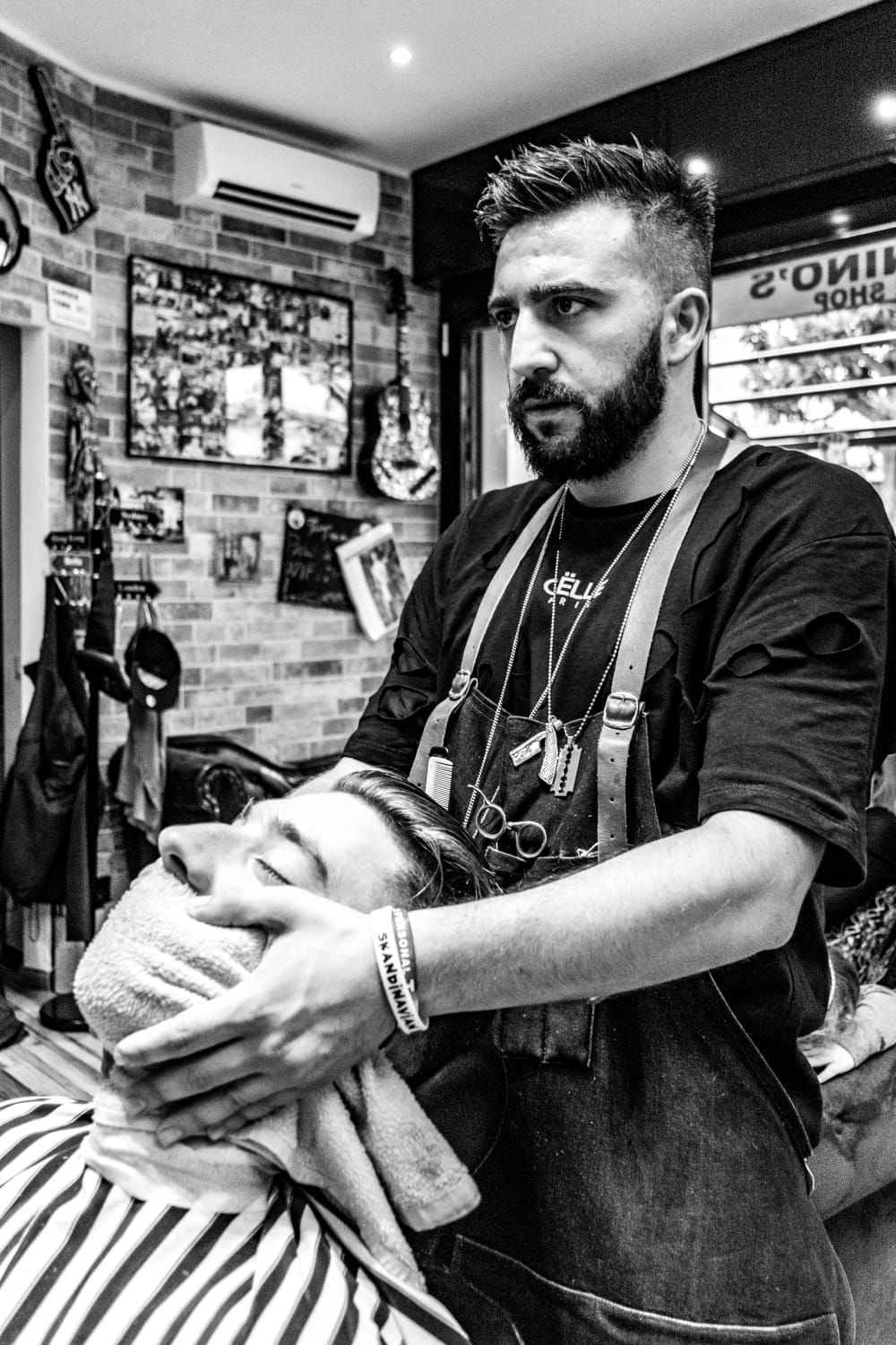 Un barbiere taglia i capelli a un cliente in una barberia, con decorazioni in bianco e nero e poster alle pareti.