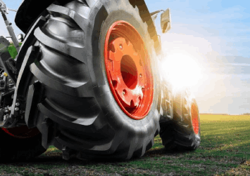 A tractor is parked in a field with the sun shining through the tires.