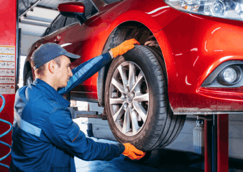 A man is changing a tire on a red car in a garage.