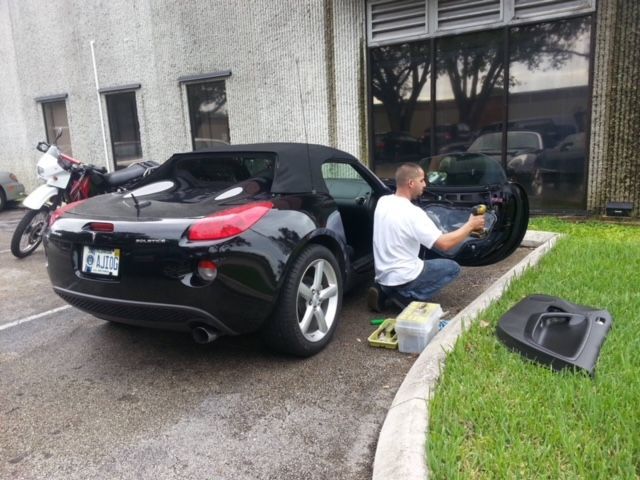 A man is kneeling in front of a black sports car with a license plate that says ' a ' on it