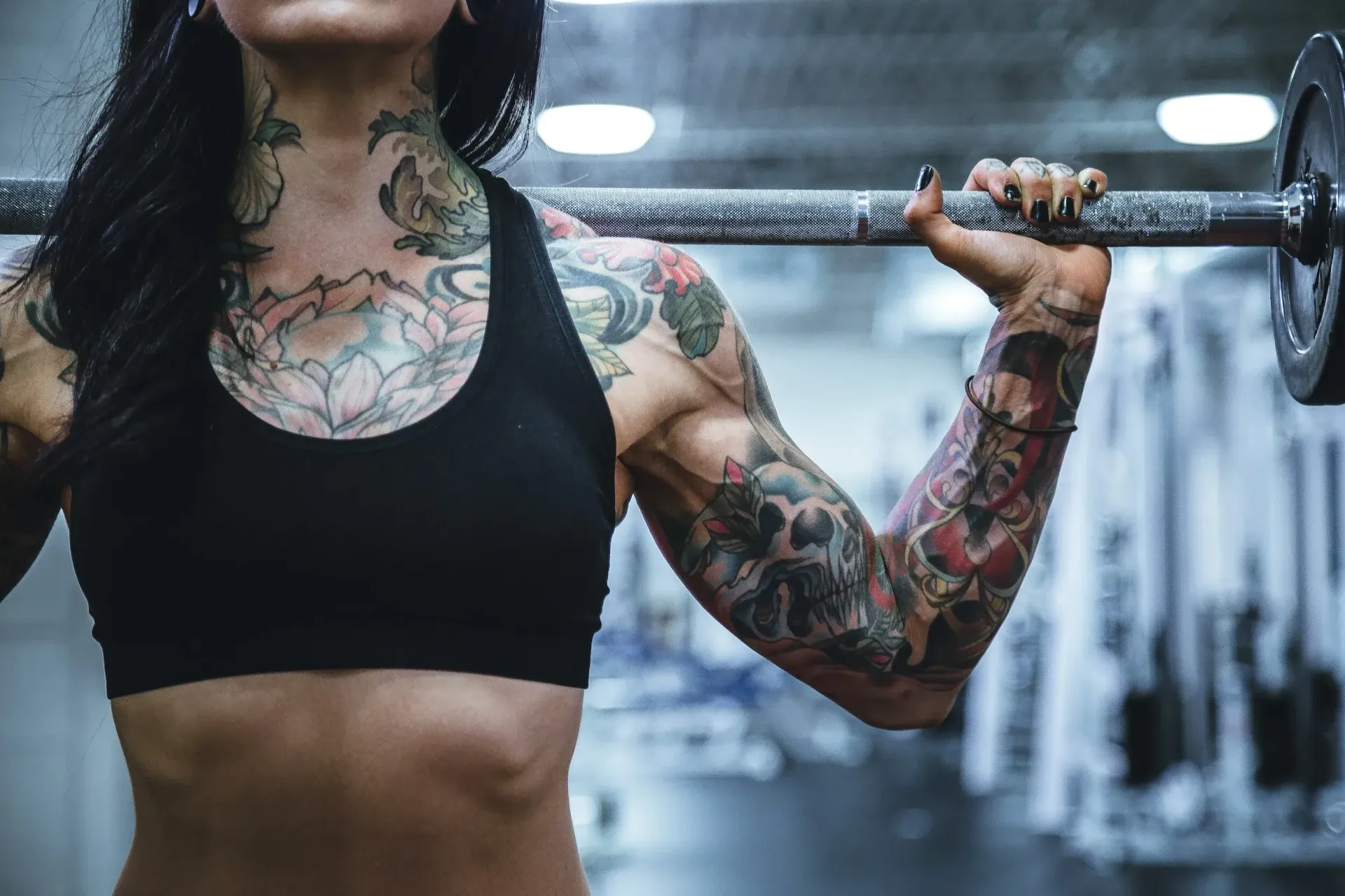 Woman with tattoos lifting a barbell in a gym in Lubbock, TX.