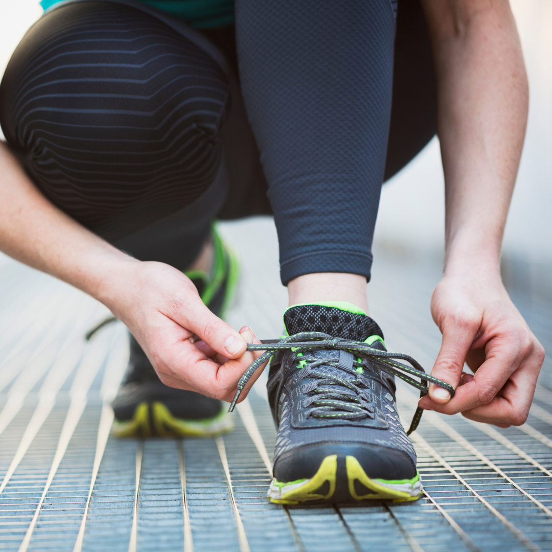 Person kneeling, tying shoelaces on running shoes with green and black accents, outdoors on a metal grate.
