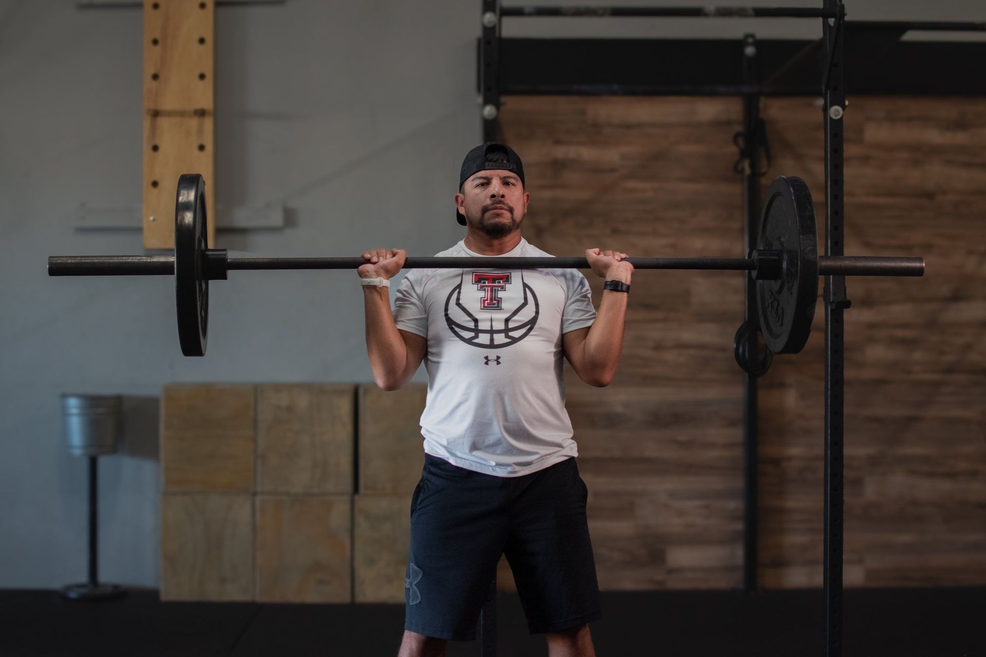 Man working out at Sweat District in Lubbock, TX, holding barbell in front of shoulders, performing front squat.