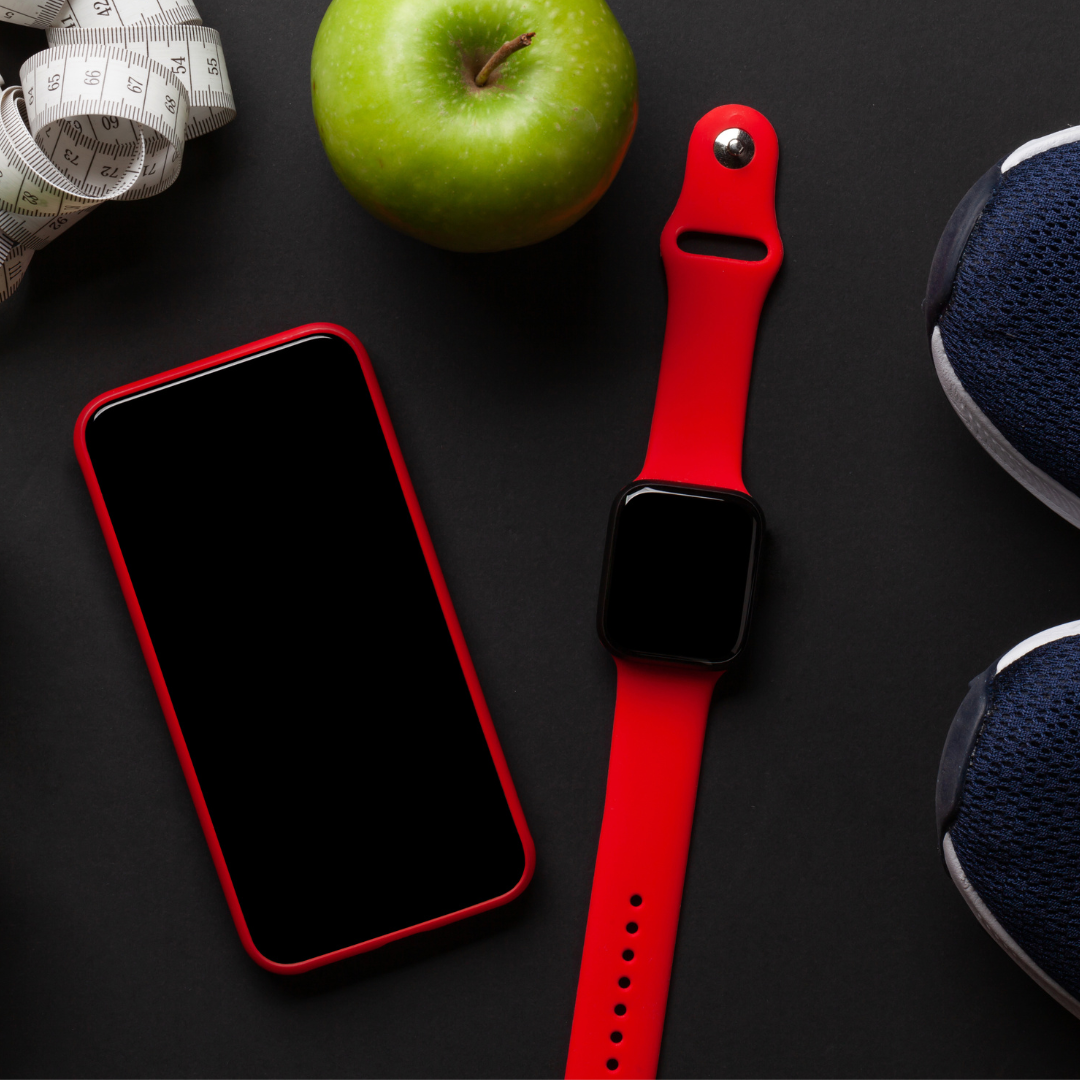 Fitness items on a black surface: red watch, phone, apple, shoes, and measuring tape.