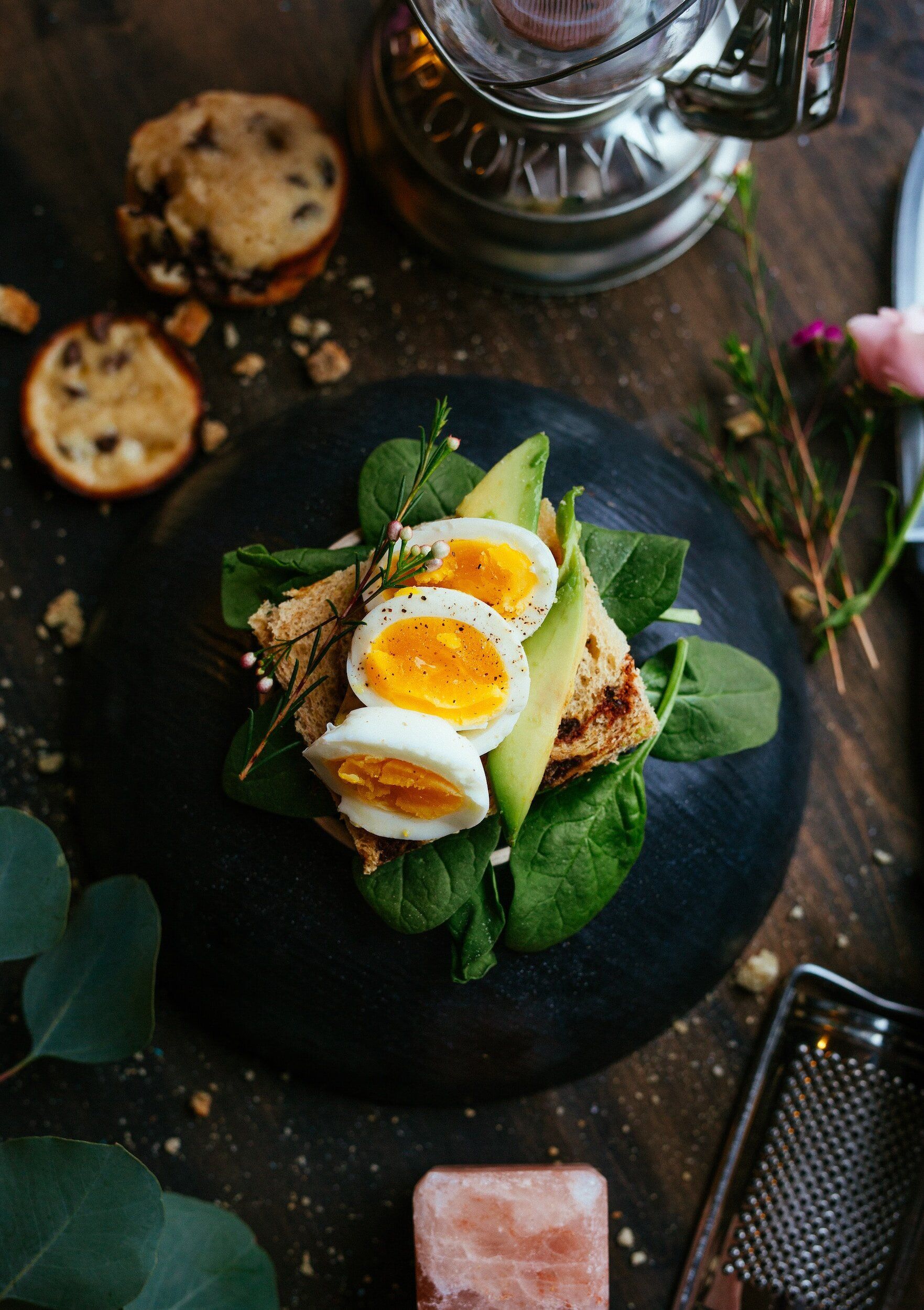 Egg and avocado toast on a dark plate, with cookies and decorative elements.