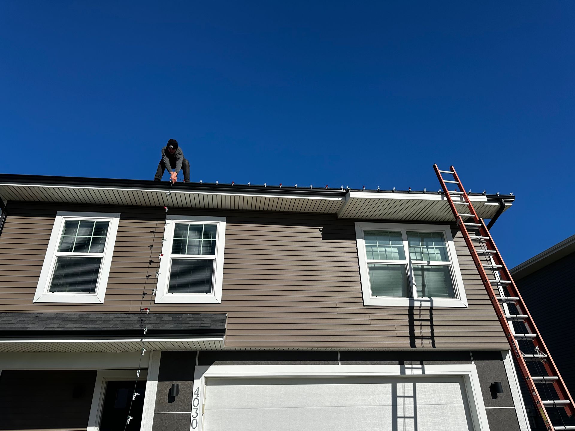 A man is standing on the roof of a house with a ladder.
