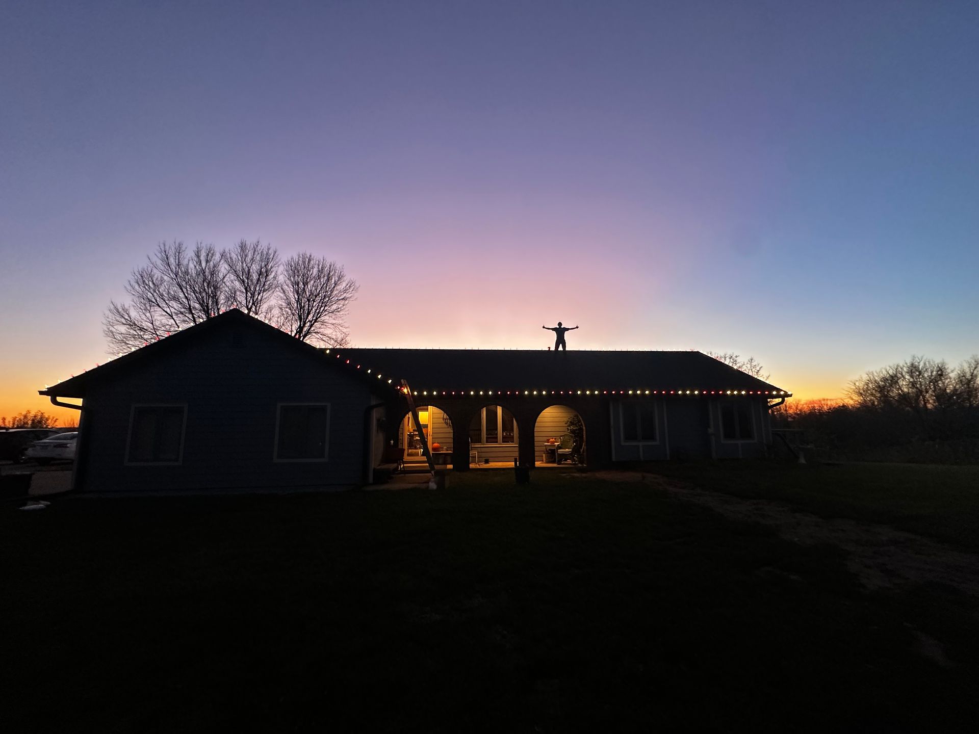 A man is standing on the roof of a house at sunset.