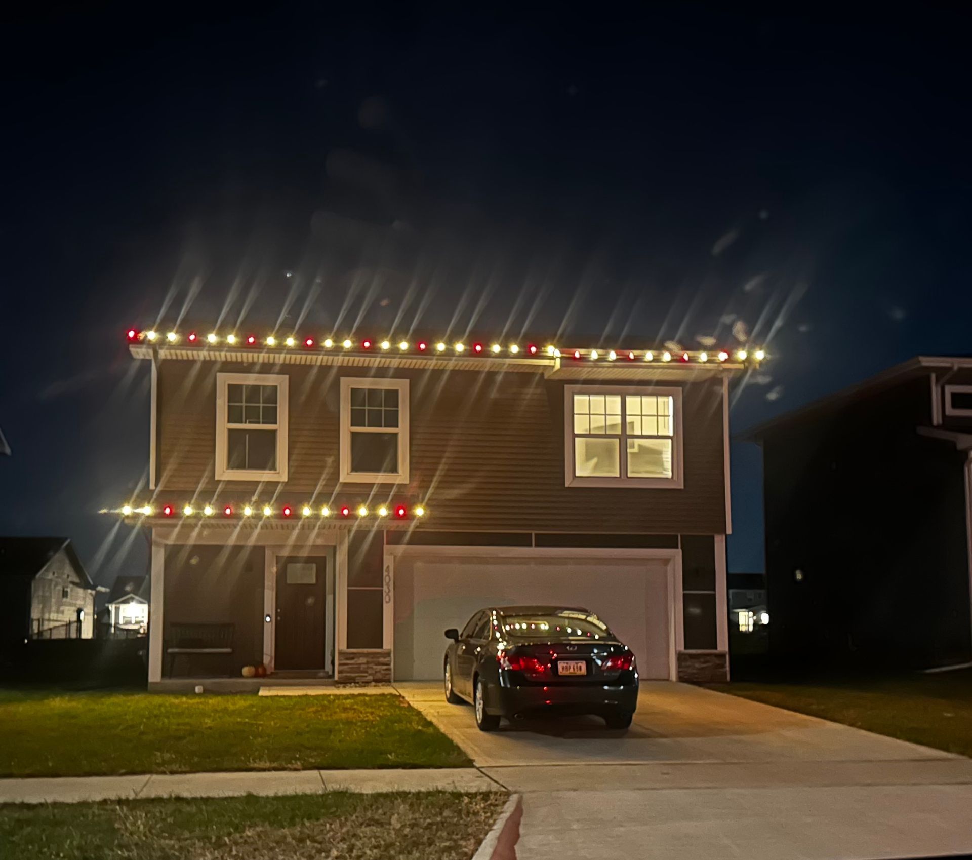 A car is parked in front of a house with christmas lights on it