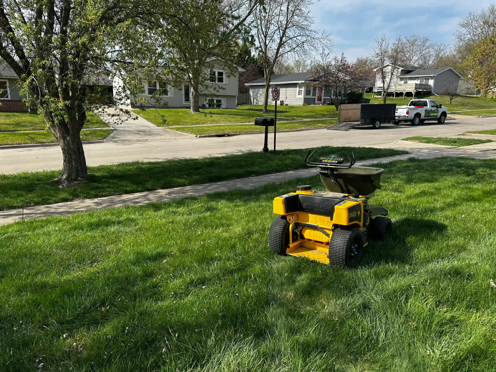 A yellow power seeder is sitting on top of a lush green lawn.