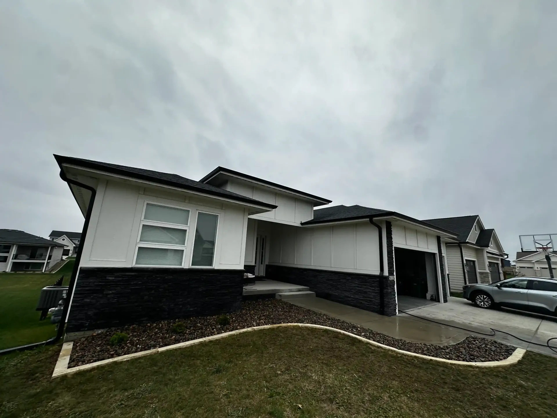 A white and black house with a car parked in front of it on a cloudy day.