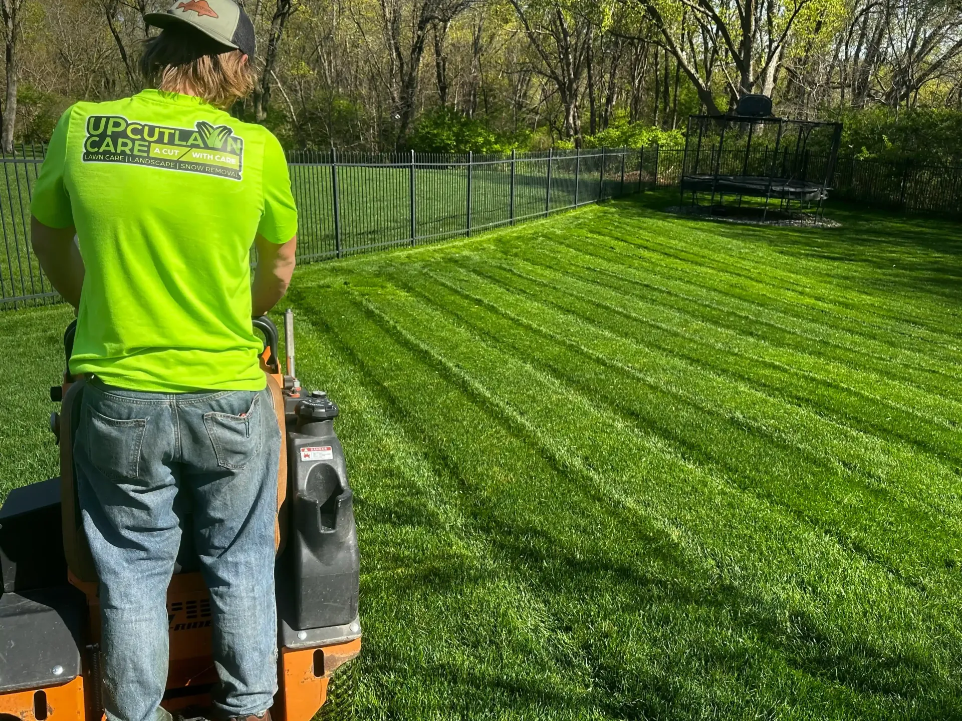 A man in a neon green shirt is mowing a lush green lawn.