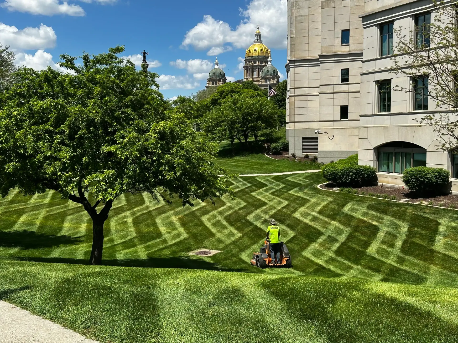 A man is mowing a lush green lawn in front of a building.