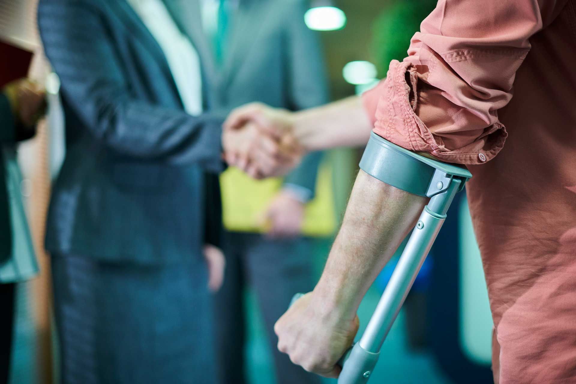 A man with crutches is shaking hands with a woman.