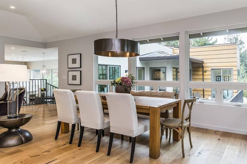 Bright dining room with white chairs, wood table, pendant light, and large windows overlooking a patio