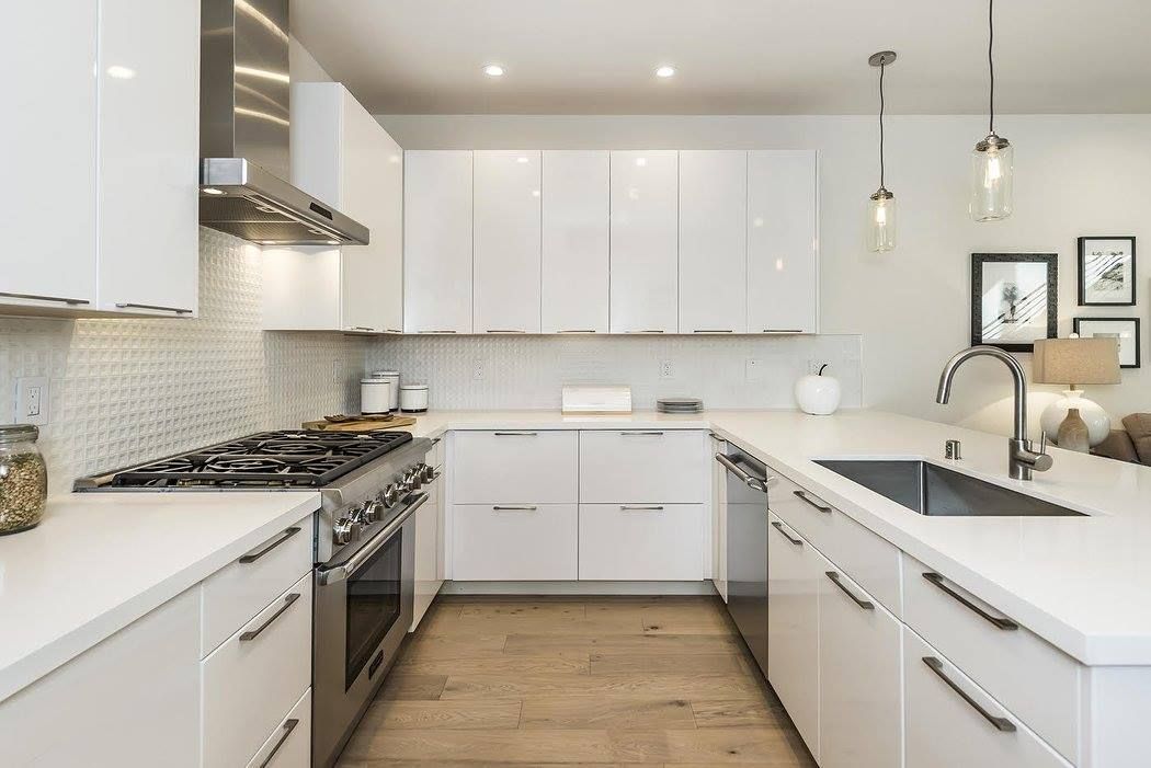 Bright modern white kitchen with stainless appliances, wood floor, and peninsula sink