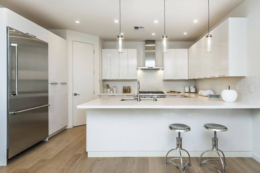 Modern white kitchen with island, stainless steel fridge, and two stools under pendant lights