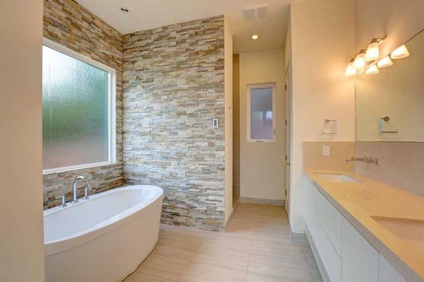 Modern bathroom with a freestanding tub, stone accent wall, and double vanity sink with mirror lights
