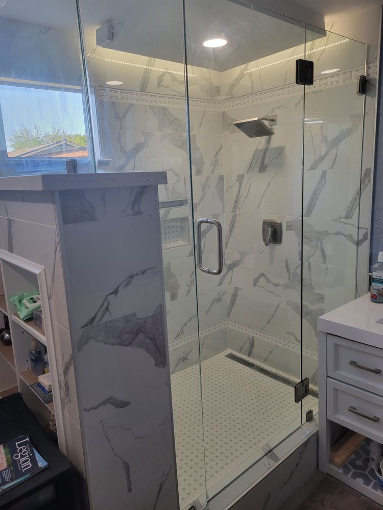 Glass shower enclosure in a marble-look bathroom with a built-in bench and shelves.