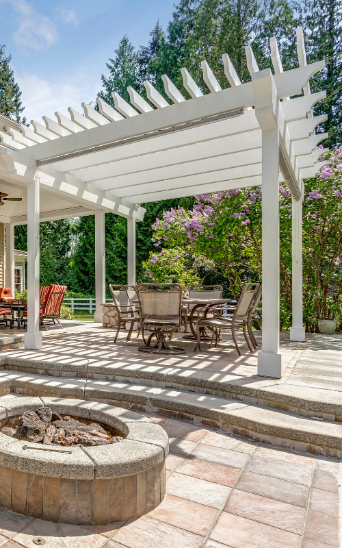 There is a fire pit in the middle of the patio under a pergola.
