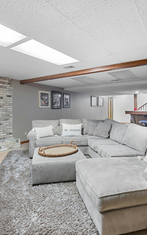 A living room with a large sectional couch , ottoman , and rug.