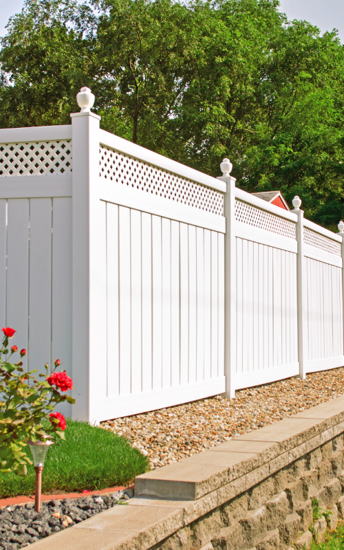 A white fence with a lattice top is next to a stone wall.