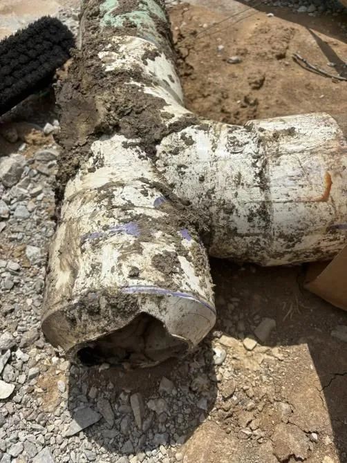 A muddy pipe is laying on the ground next to a tire.