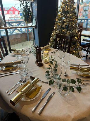 Christmas dinner table laid up for food, with a decorated Christmas tree in the background.