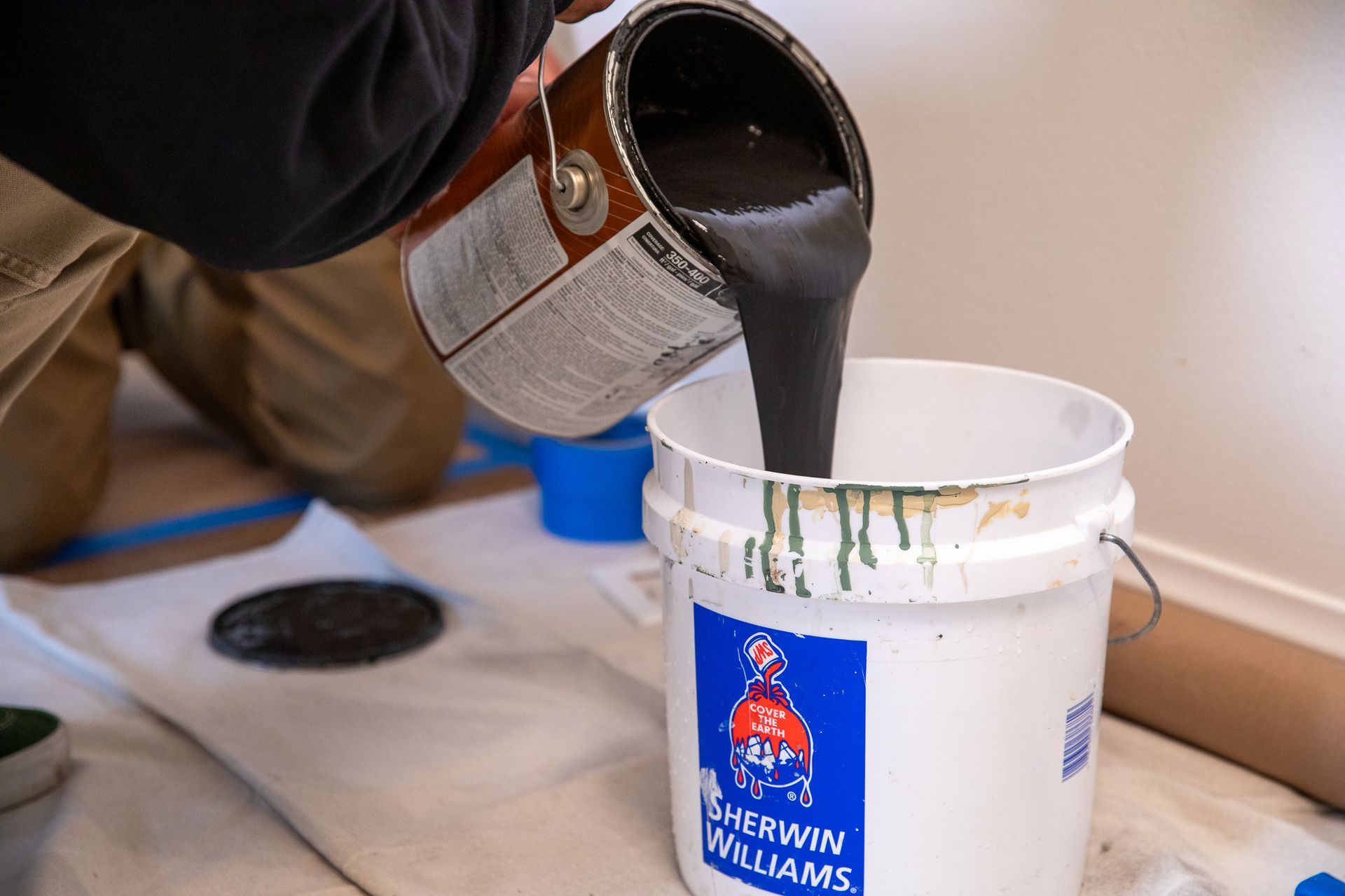 a person is pouring paint into a bucket from a can .