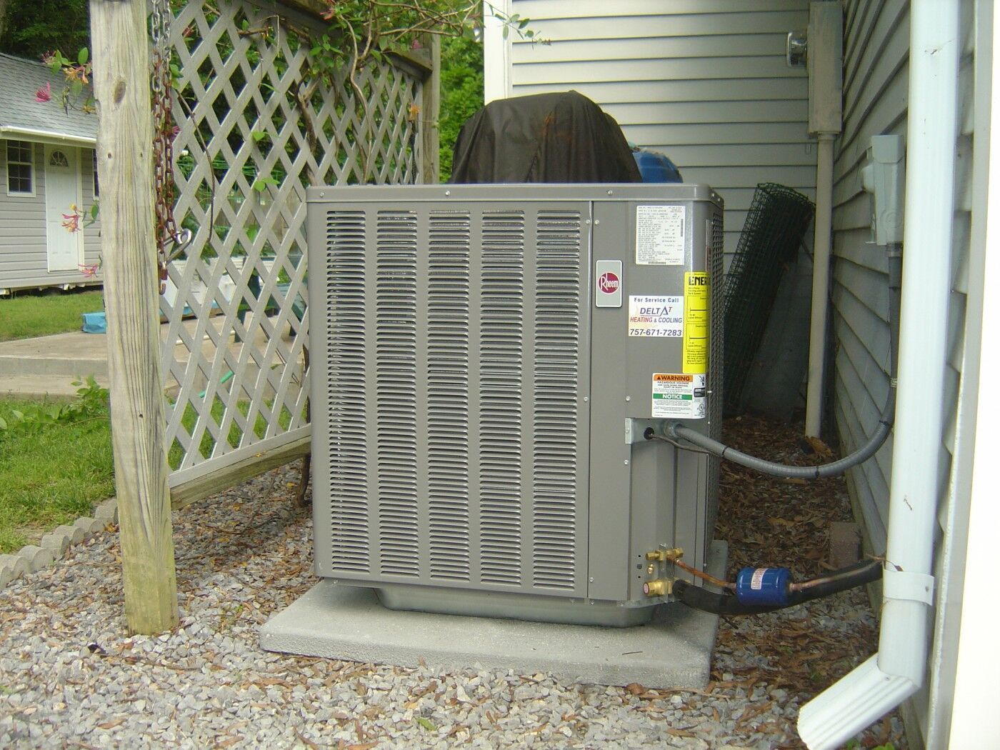 A gray air conditioner is sitting outside of a house