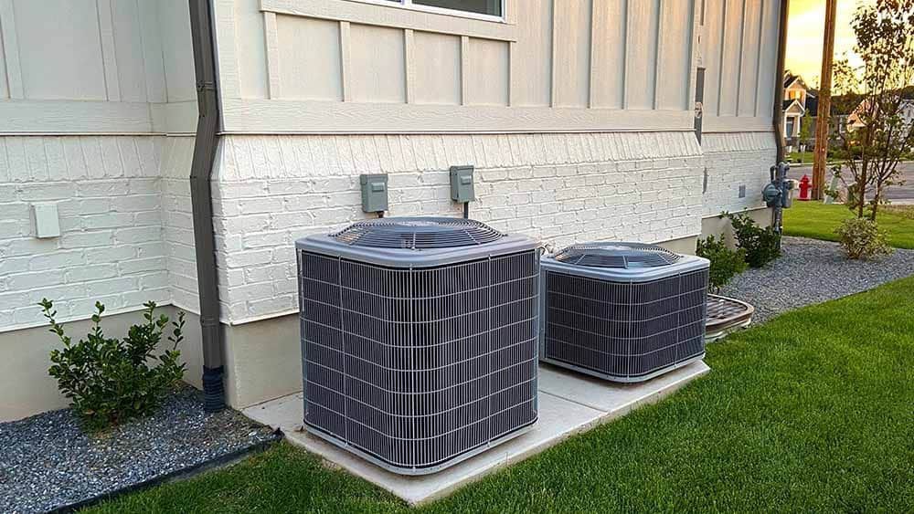 Two air conditioners are sitting on the side of a house.