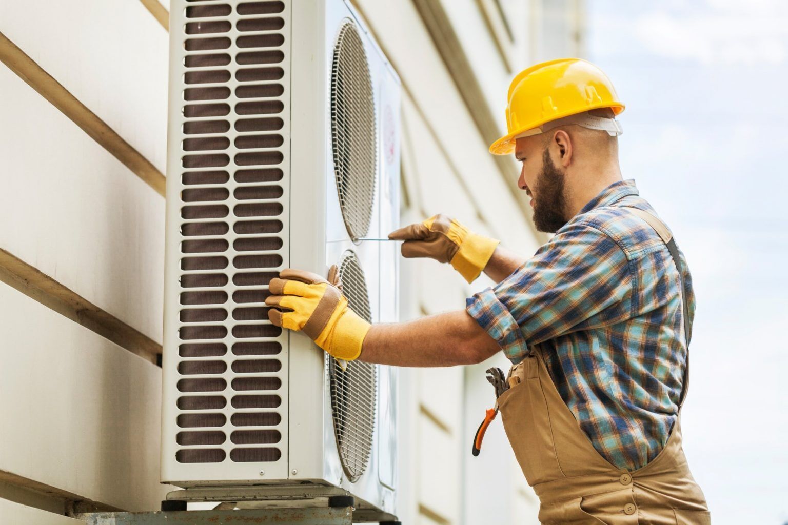 A man is installing an air conditioner on the side of a building.